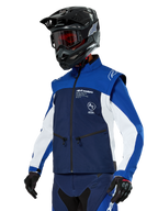 Giacca Softshell Alpinestars Lite-Dura, blu navy, azzurro e bianco, giacca da enduro off-road, indossata con casco nero e occhiali con lenti rosse, design sportivo color-block con cerniere multiple e loghi del brand, tessuto resistente per motocross e trail riding