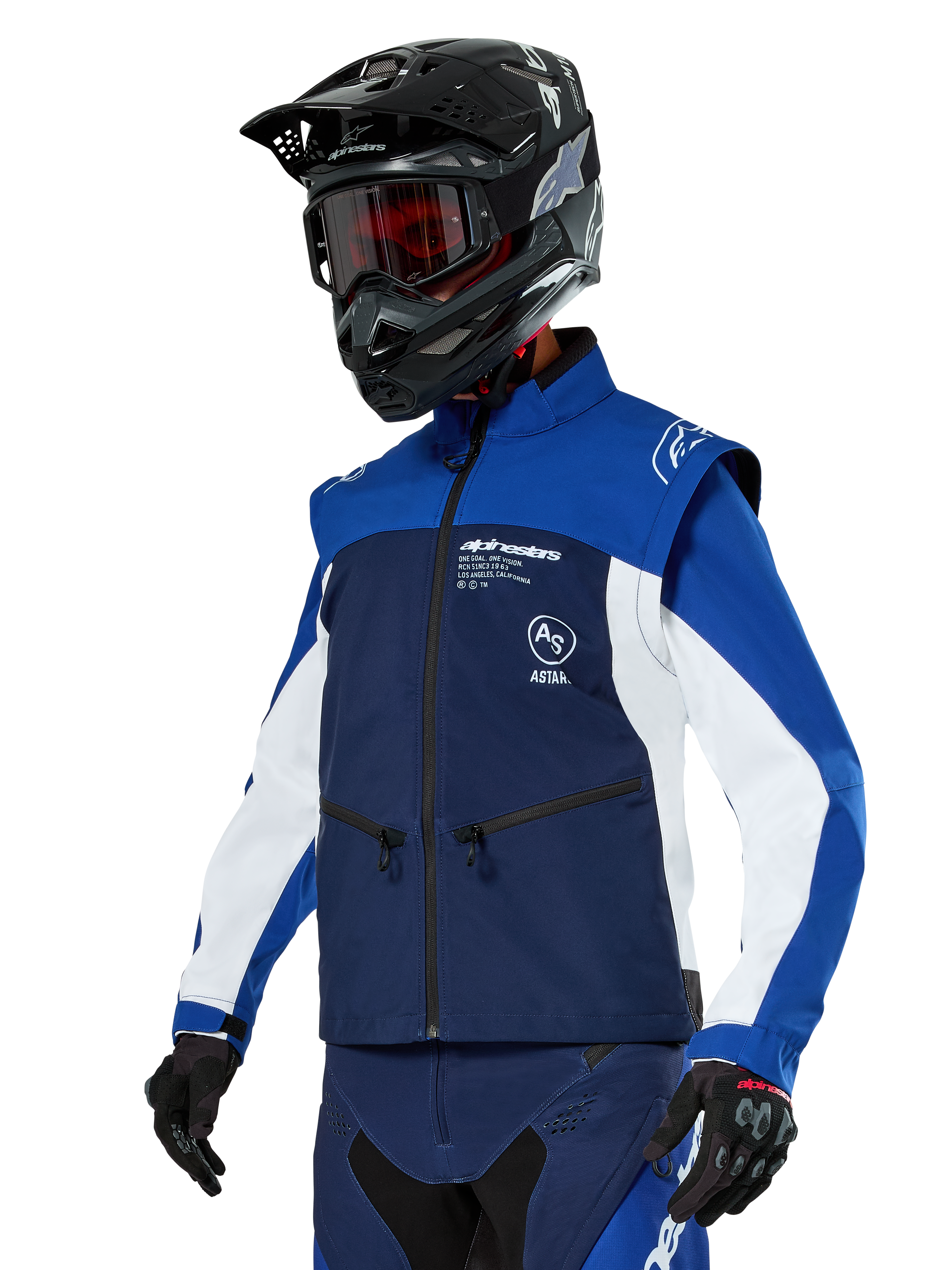 Giacca Softshell Alpinestars Lite-Dura, blu navy, azzurro e bianco, giacca da enduro off-road, indossata con casco nero e occhiali con lenti rosse, design sportivo color-block con cerniere multiple e loghi del brand, tessuto resistente per motocross e trail riding