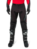 Pantaloni Alpinestars Pro-Dura, pantaloni da enduro neri e magnet, indossati con una maglia rossa a maniche lunghe e stivali da motocross neri, caratterizzati dal marchio Alpinestars grigio e dalla robusta costruzione in ripstop per la guida fuori strada