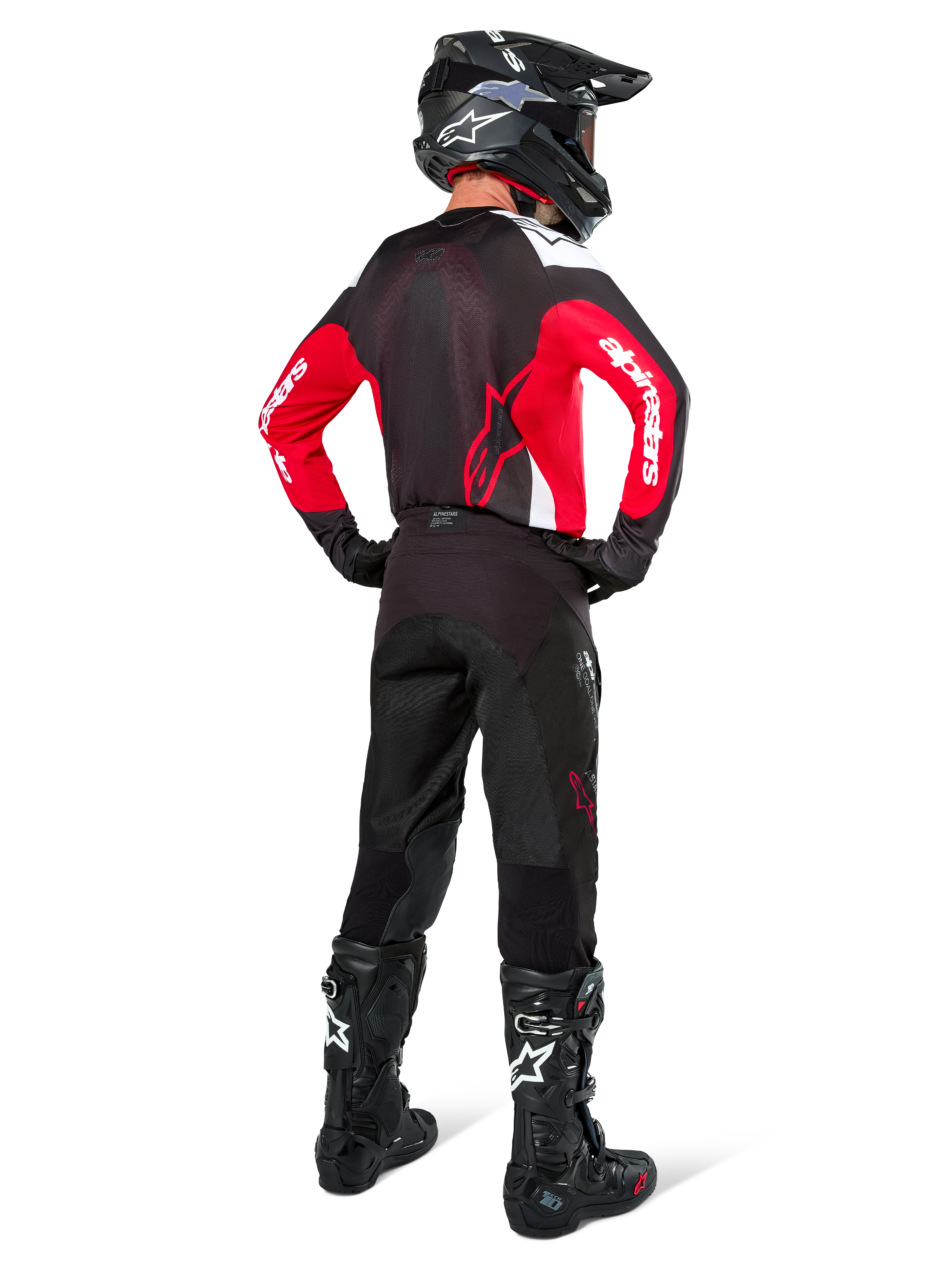 Pilota di motocross visto da dietro che indossa i pantaloni Alpinestars Pro-Dura in Black Magnet White, abbinati a una maglia rossa e nera e stivali neri, set di abbigliamento off-road coordinato per la guida enduro