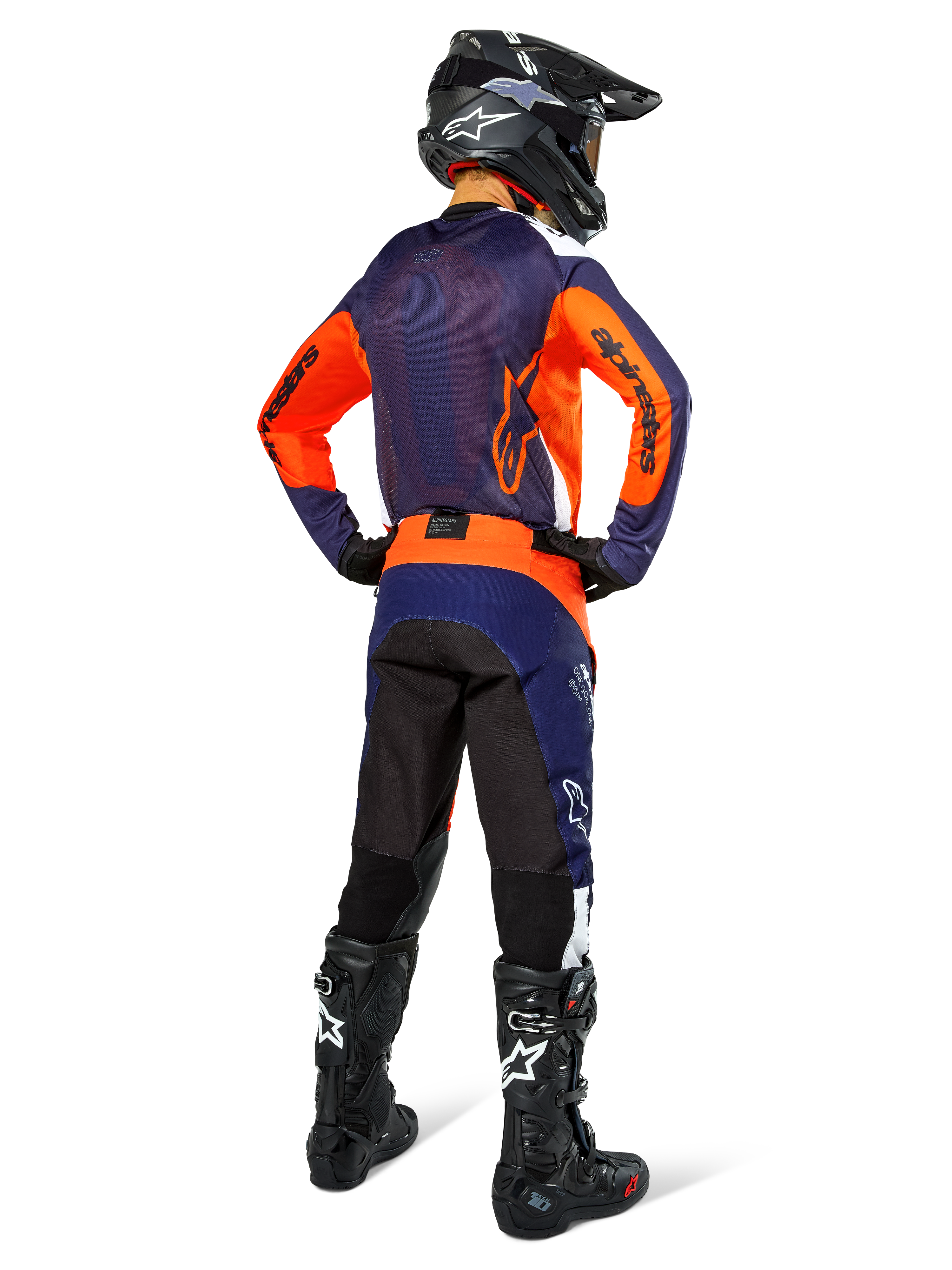 Pilota di motocross con abbigliamento da gara completo visto di spalle, maglia blu navy e arancione, pantaloni Pro-Dura in Navy Hot Orange White, casco e stivali neri, completo professionale da corsa off-road.