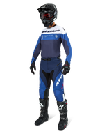Pilota di motocross che indossa pantaloni Alpinestars Pro-Dura in Blu Navy, Blu Brillante e Bianco, abbinati a una maglia a maniche lunghe coordinata, casco nero con occhiali rossi, guanti neri e stivali bianchi e neri, completo coordinato per enduro e gare fuoristrada.