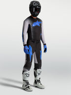 Pantaloni Alpinestars Supertech Hiten AFD, pantaloni da motocross neri e blu, indossati con maglia coordinata e stivali bianchi.