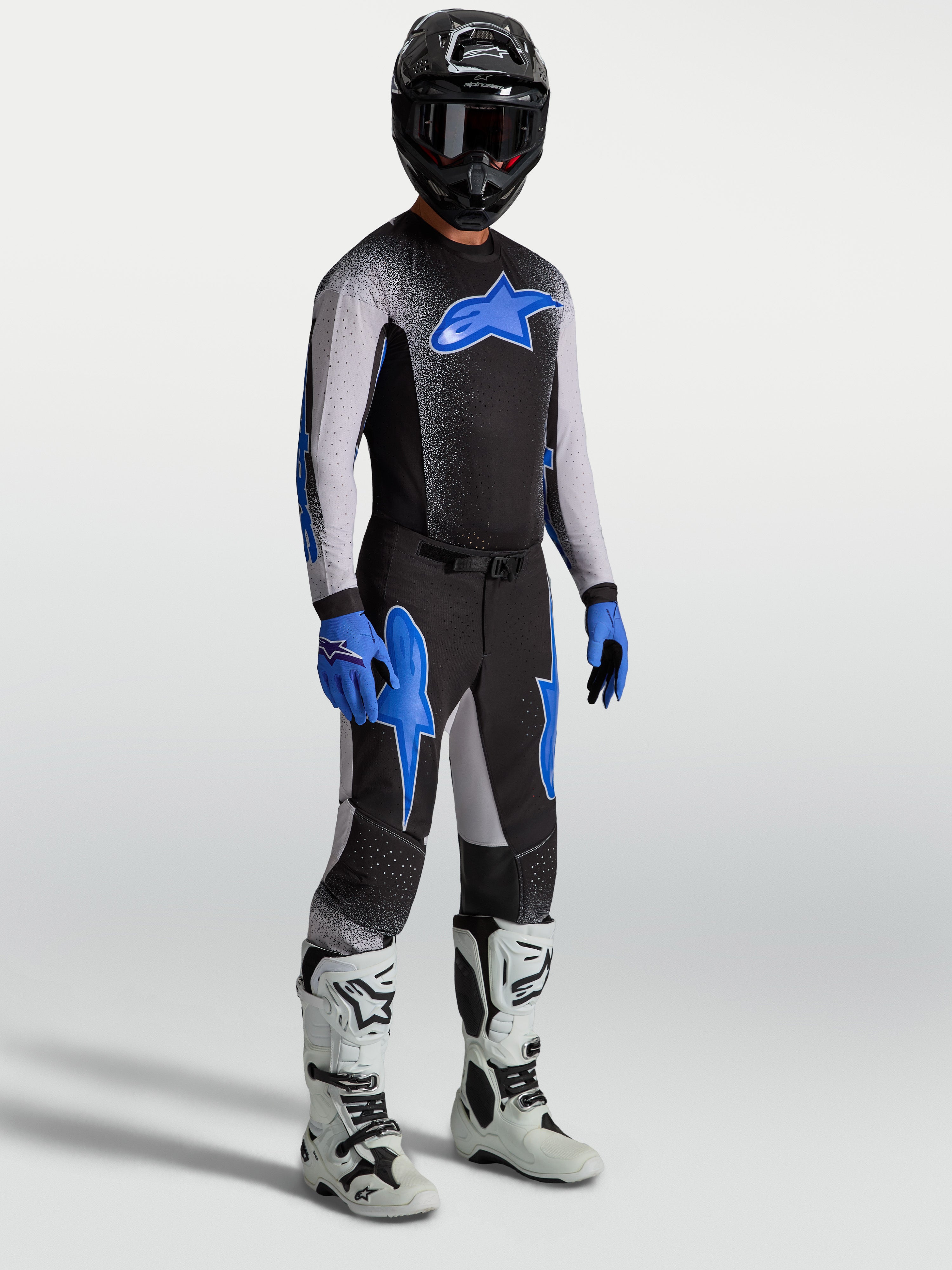 Pantaloni Alpinestars Supertech Hiten AFD, pantaloni da motocross neri e blu, indossati con maglia coordinata e stivali bianchi.