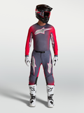 Alpinestars Supertech Hiten AFD Gear Set e Pantaloni, completo professionale da motocross per uomo, grigio e rosso fluo, maglia e pantaloni tecnici indossati con casco e stivali.