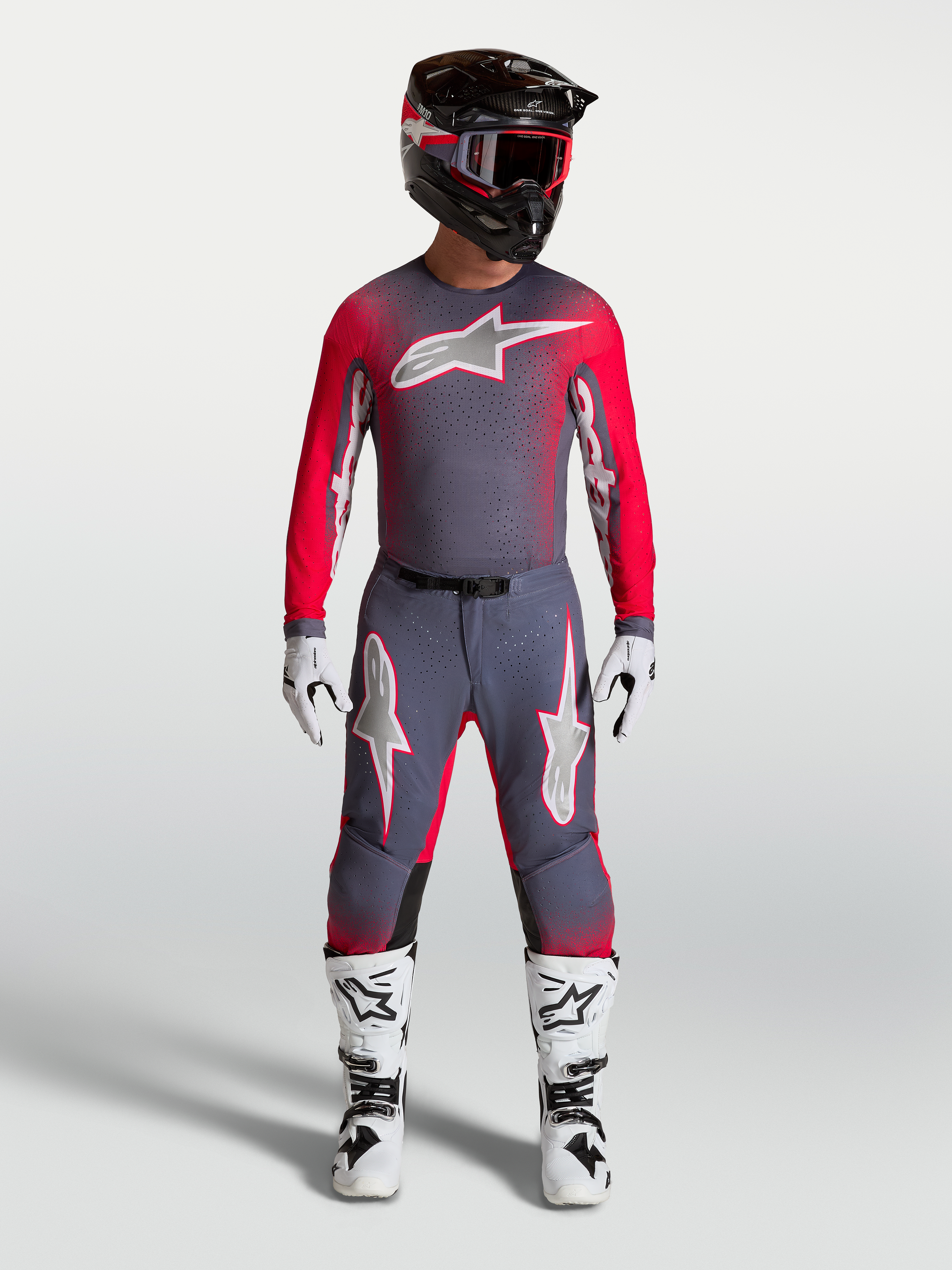 Alpinestars Supertech Hiten AFD Gear Set e Pantaloni, completo professionale da motocross per uomo, grigio e rosso fluo, maglia e pantaloni tecnici indossati con casco e stivali.