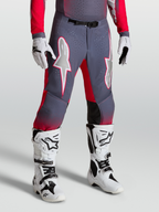 Alpinestars Pantaloni Supertech Hiten AFD, pantaloni da motocross grigi e rossi con grafiche a stella e fibbia magnetica, indossati con stivali bianchi.