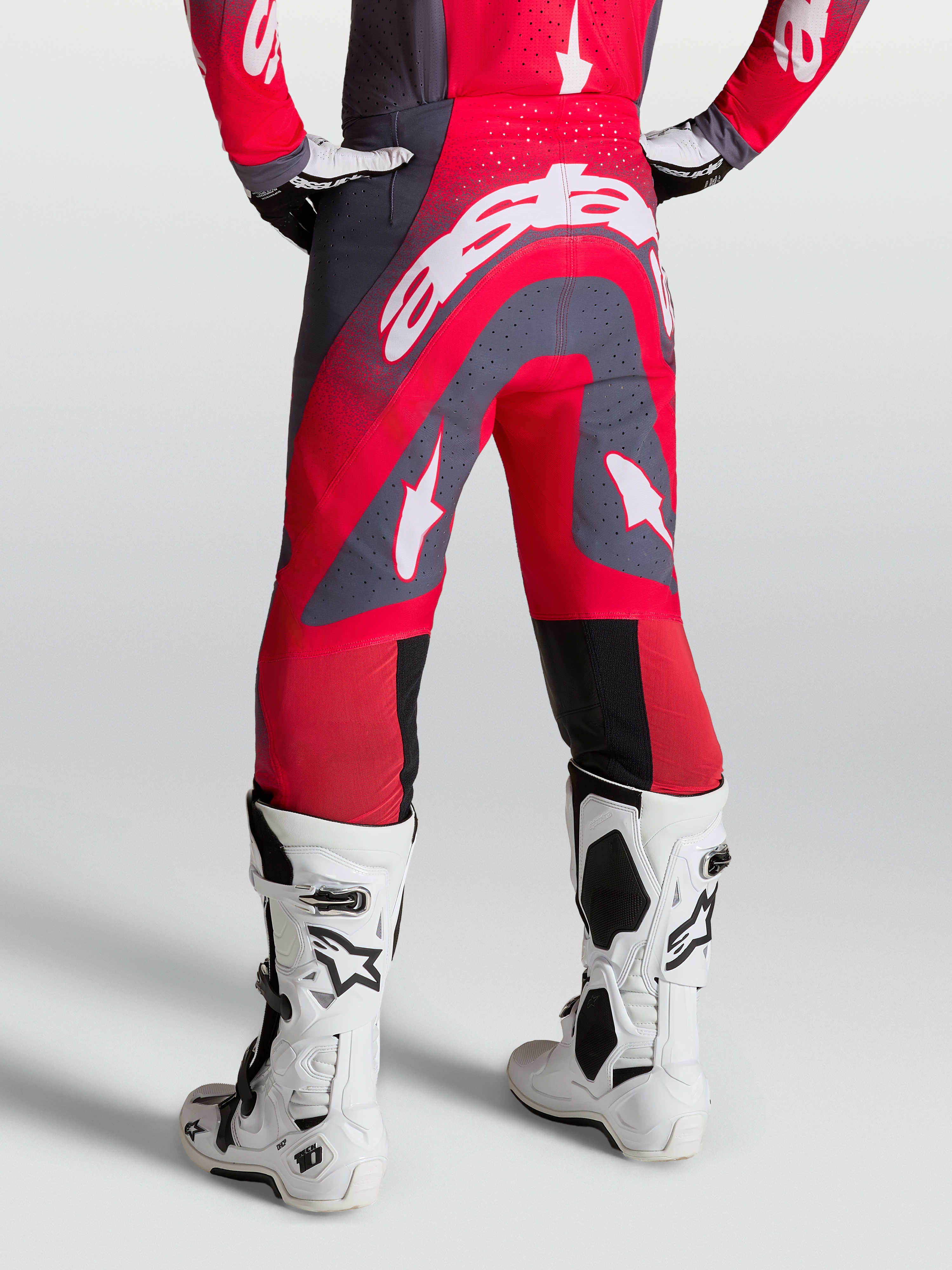 Alpinestars Pantaloni Supertech Hiten AFD, pantaloni da motocross rossi e grigi, vista posteriore su modello con stivali racing bianchi.