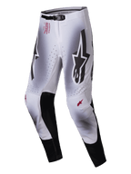Alpinestars 2025 Supertech Maker Pants, pantaloni da motocross, argento e nero, con grandi loghi Astars neri sulle cosce, branding tecnico rosso sull'anca, pannelli interni in pelle nera sulle ginocchia e zone di ventilazione perforate.