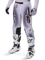 Alpinestars 2025 Supertech Maker Pants, pantaloni da motocross, argento e nero, con grandi loghi a stella e scritte rosse, mostrati con stivali e guanti bianchi coordinati