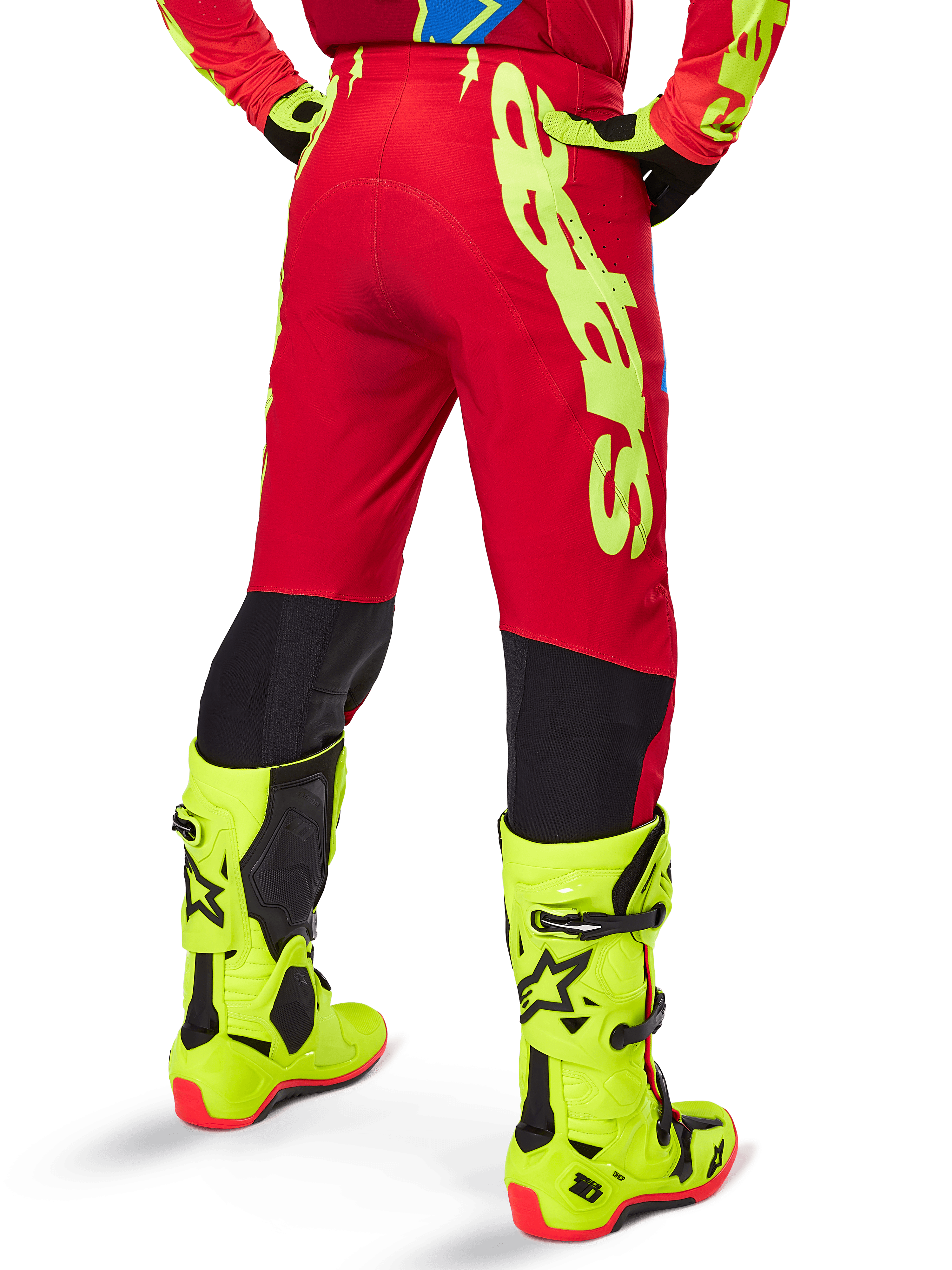 Alpinestars 2025 Supertech Maker Pants, pantaloni da motocross, rosso acceso e giallo fluo, vista posteriore che mostra il grande logo giallo sul lato e i pannelli neri sulla parte inferiore delle gambe, indossati con stivali e attrezzatura giallo fluo coordinati