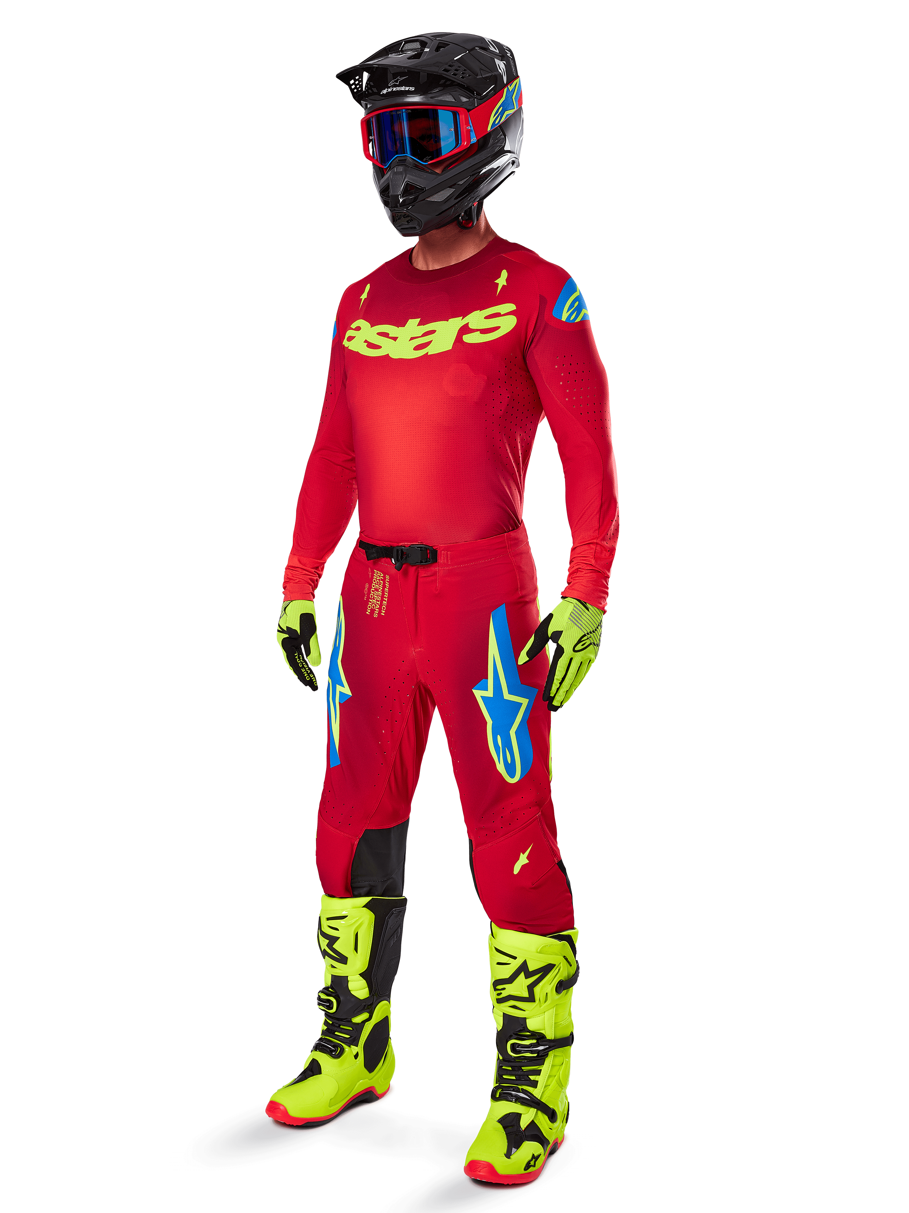 Pilota di motocross con abbigliamento completo Alpinestars, pantaloni Supertech Maker 2025 in rosso acceso e giallo fluo, maglia rossa coordinata con logo giallo neon, stivali giallo neon e neri, casco nero con occhiali blu, outfit professionale per gare fuoristrada