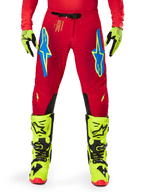 Alpinestars 2025 Supertech Maker Pants, pantaloni da motocross, rosso brillante e giallo fluo, con loghi Astars blu sulle cosce, perforazioni per la ventilazione e pannelli interni delle ginocchia neri, indossati con stivali e guanti giallo fluo coordinati