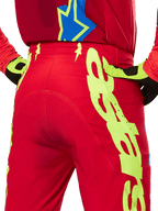Alpinestars 2025 Supertech Maker Pants, pantaloni da motocross, rosso acceso e giallo fluo, vista posteriore con ampie grafiche gialle sulle gambe e guanti coordinati giallo fluo e nero, abbigliamento professionale da gara fuoristrada