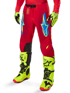 Alpinestars Pantaloni Supertech Maker 2025, pantaloni da motocross, rosso acceso con loghi a stella blu e gialli, pannelli neri sulle ginocchia, ventilazione traforata, coordinati con stivali e guanti giallo neon