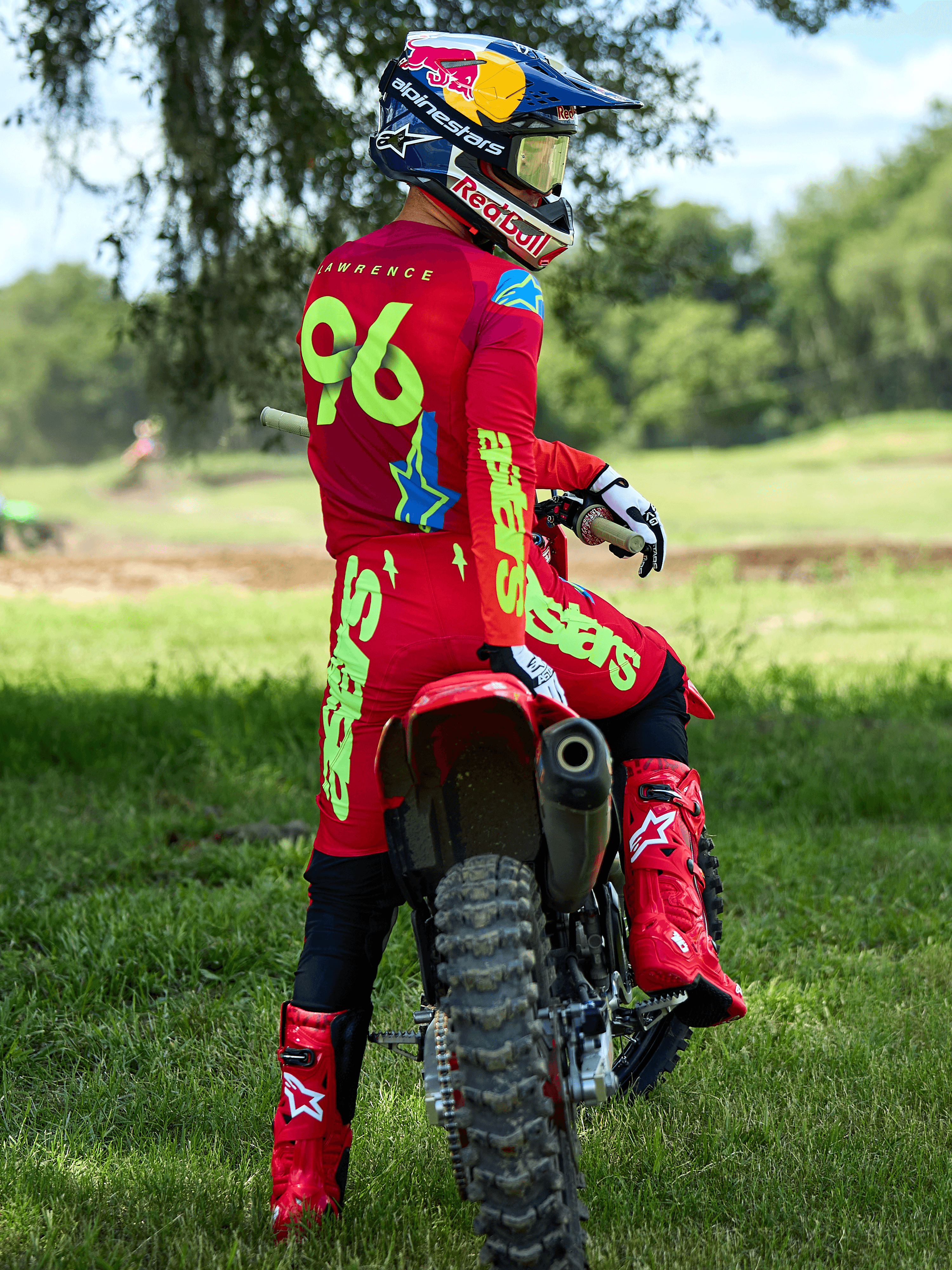 Pilota di motocross seduto su una moto da cross rossa, pantaloni Alpinestars 2025 Supertech Maker in rosso vivace e giallo fluo, maglia rossa coordinata con '96' e 'LAWRENCE' sul retro, stivali da gara rossi e casco marchiato Red Bull, set di abbigliamento professionale da gara fuoristrada