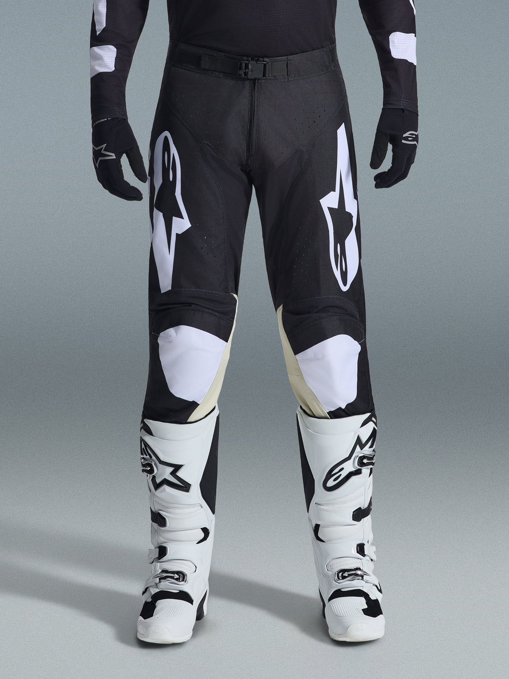 Alpinestars 2026 Racer Air Riway Pants, pantaloni da motocross, nero e bianco, con vistosi loghi Alpinestars bianchi sulle cosce e sui pannelli delle ginocchia, abbinati a stivali da motocross bianchi e neri e guanti neri, design atletico race-fit per la guida off-road