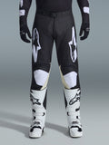 Alpinestars 2026 Racer Air Riway Pants, pantaloni da motocross, nero e bianco, con vistosi loghi Alpinestars bianchi sulle cosce e sui pannelli delle ginocchia, abbinati a stivali da motocross bianchi e neri e guanti neri, design atletico race-fit per la guida off-road