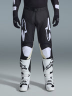 Alpinestars 2026 Racer Air Riway Pants, pantaloni da motocross, nero e bianco, con vistosi loghi Alpinestars bianchi sulle cosce e sui pannelli delle ginocchia, abbinati a stivali da motocross bianchi e neri e guanti neri, design atletico race-fit per la guida off-road