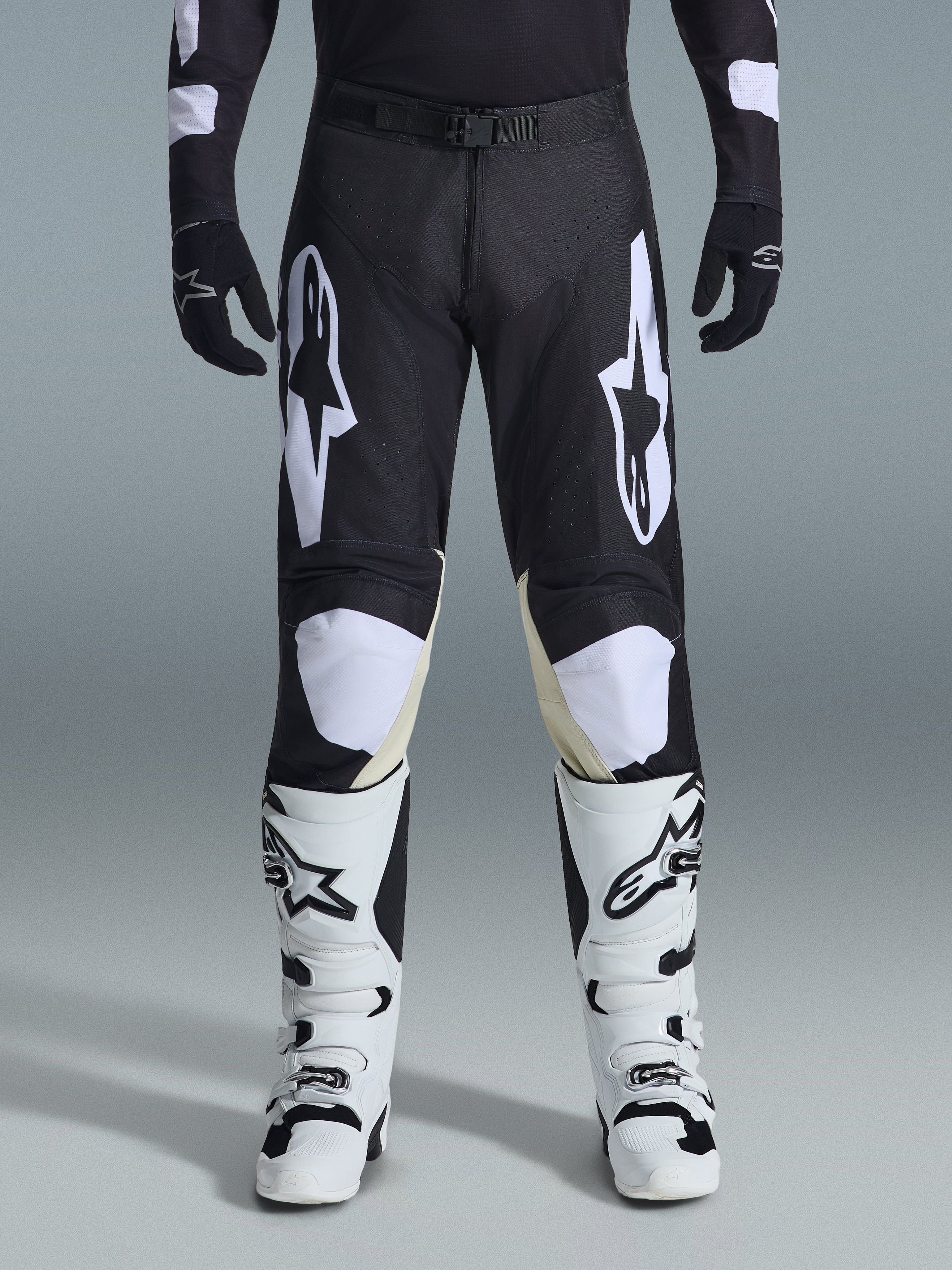 Alpinestars 2026 Racer Air Riway Pants, pantaloni da motocross, nero e bianco, con vistosi loghi Alpinestars bianchi sulle cosce e sui pannelli delle ginocchia, abbinati a stivali da motocross bianchi e neri e guanti neri, design atletico race-fit per la guida off-road