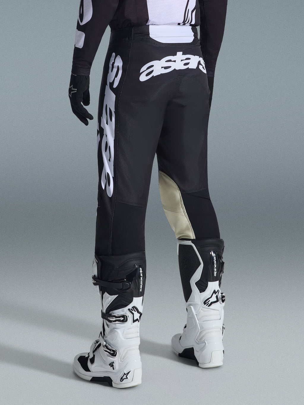 Alpinestars 2026 Racer Air Riway Pants, pantaloni da motocross, bianco e nero, vista posteriore con grande marchio Astars bianco sulla seduta e sulle gambe, pannelli interni del ginocchio in pelle tan, indossati con stivali Tech 7 bianchi e neri, abbigliamento premium per corse fuoristrada
