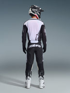 Pilota di motocross visto da dietro con pantaloni Alpinestars 2026 Racer Air Riway in nero e bianco, maglia coordinata a maniche lunghe nera e bianca, stivali da corsa bianchi e neri e casco nero con branding Alpinestars.