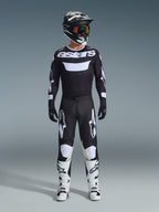 Pilota di motocross con pantaloni Alpinestars 2026 Racer Air Riway in nero e bianco, maglia coordinata nera e bianca con logo 'astars', casco nero, occhiali con lenti iridescenti e stivali da corsa bianchi, completo professionale da fuoristrada