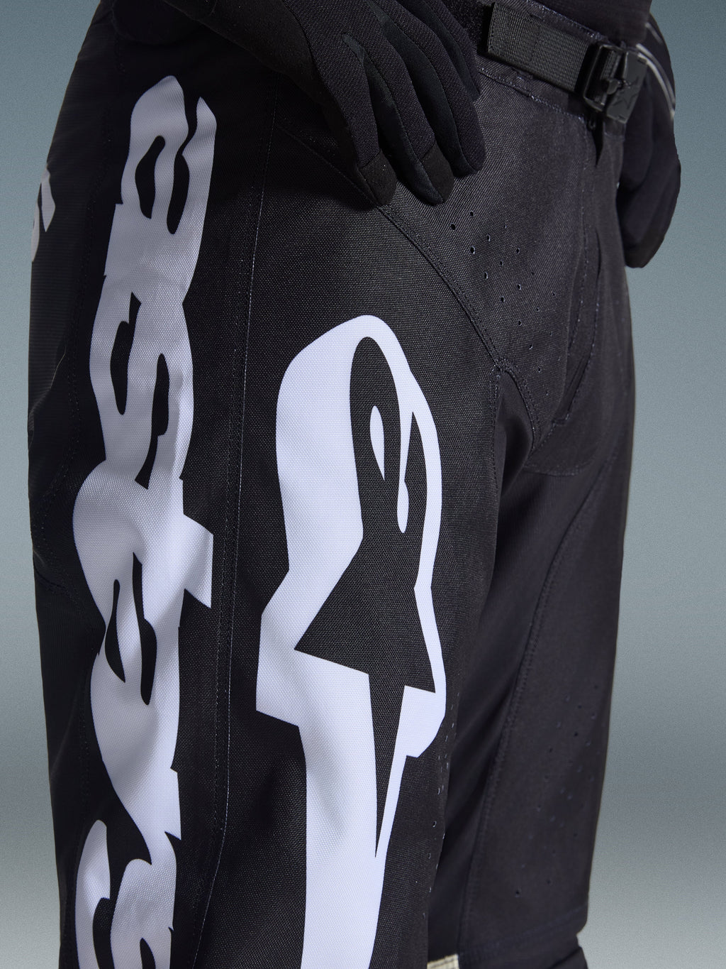 Pantaloni Alpinestars 2026 Racer Air Riway, pantaloni da motocross, nero e bianco, vista ravvicinata con grande logo Alpinestars bianco, perforazioni laser per la ventilazione e fibbia regolabile in vita, tessuto resistente per la guida fuoristrada