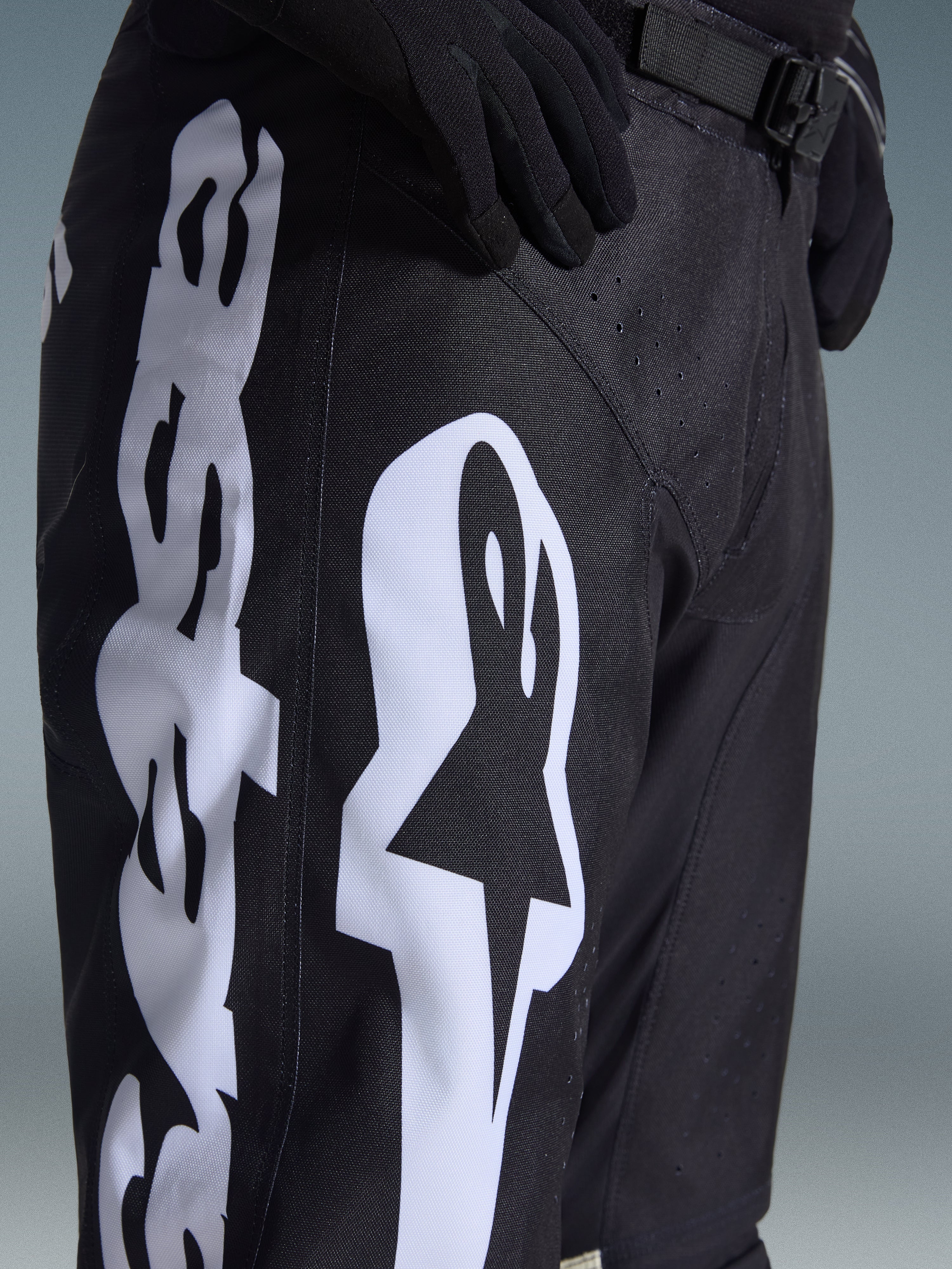 Pantaloni Alpinestars 2026 Racer Air Riway, pantaloni da motocross, nero e bianco, vista ravvicinata con grande logo Alpinestars bianco, perforazioni laser per la ventilazione e fibbia regolabile in vita, tessuto resistente per la guida fuoristrada