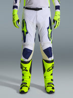 Alpinestars 2026 Racer Air Riway Pants, pantaloni da motocross, grigio chiaro, giallo fluo e blu, indossati con guanti e stivali giallo neon coordinati, con pannelli frontali traforati per il flusso d'aria e loghi vistosi blu e giallo, design atletico per prestazioni off-road