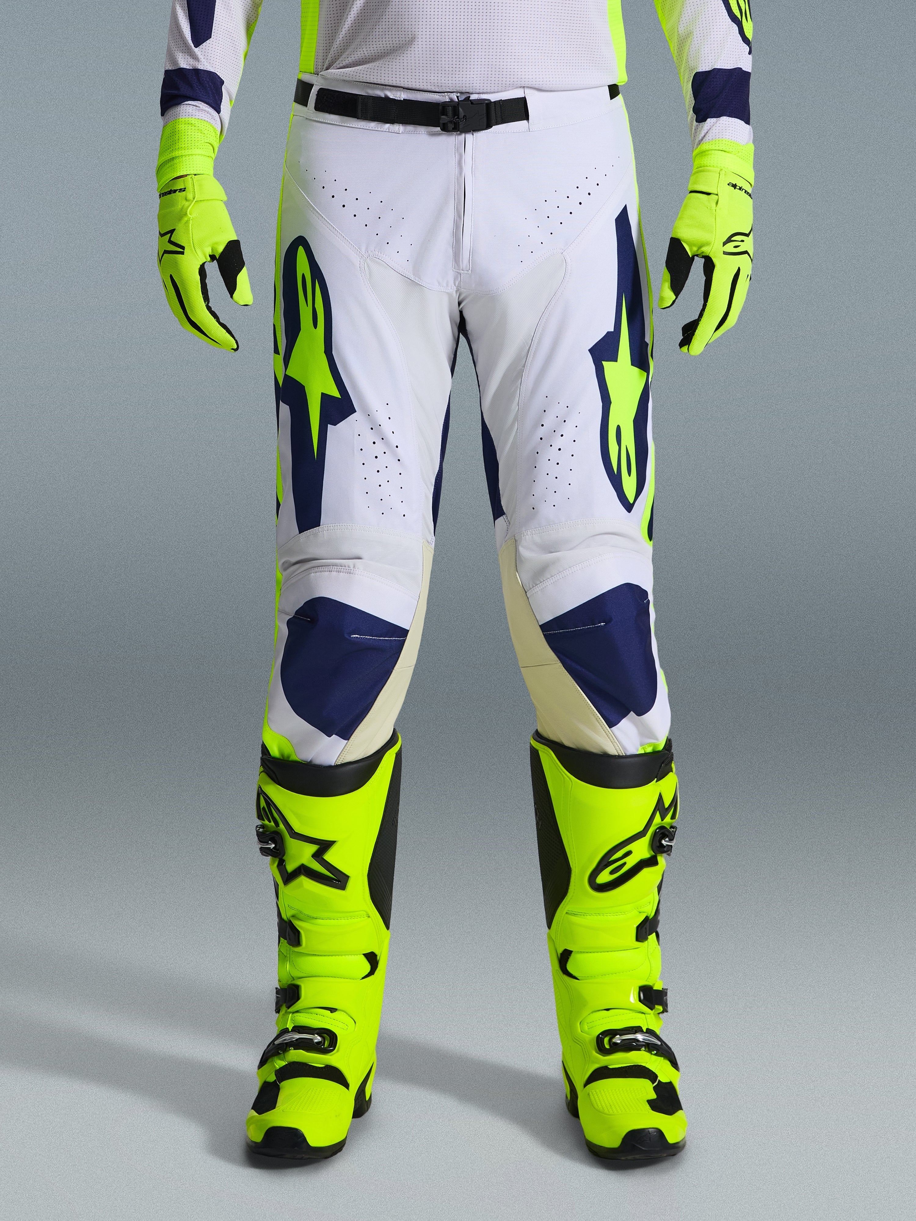 Alpinestars 2026 Racer Air Riway Pants, pantaloni da motocross, grigio chiaro, giallo fluo e blu, indossati con guanti e stivali giallo neon coordinati, con pannelli frontali traforati per il flusso d'aria e loghi vistosi blu e giallo, design atletico per prestazioni off-road