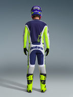 Pilota di motocross visto da dietro che indossa i pantaloni Alpinestars 2026 Racer Air Riway in grigio chiaro, giallo fluo e blu, abbinati a una maglia coordinata e stivali giallo brillante, per un set completo da gara off-road professionale.