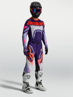 Alpinestars Pantaloni Supertech Dyna, pantaloni motocross uomo viola e rosa fluo, con maglia coordinata e stivali bianchi.