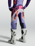 Alpinestars Pantaloni Supertech Dyna, pantaloni da motocross per uomo, viola e rosa fluo, in tessuto ripstop elastico e traspirante, vestibilità atletica, vista posteriore indossati con stivali bianchi.