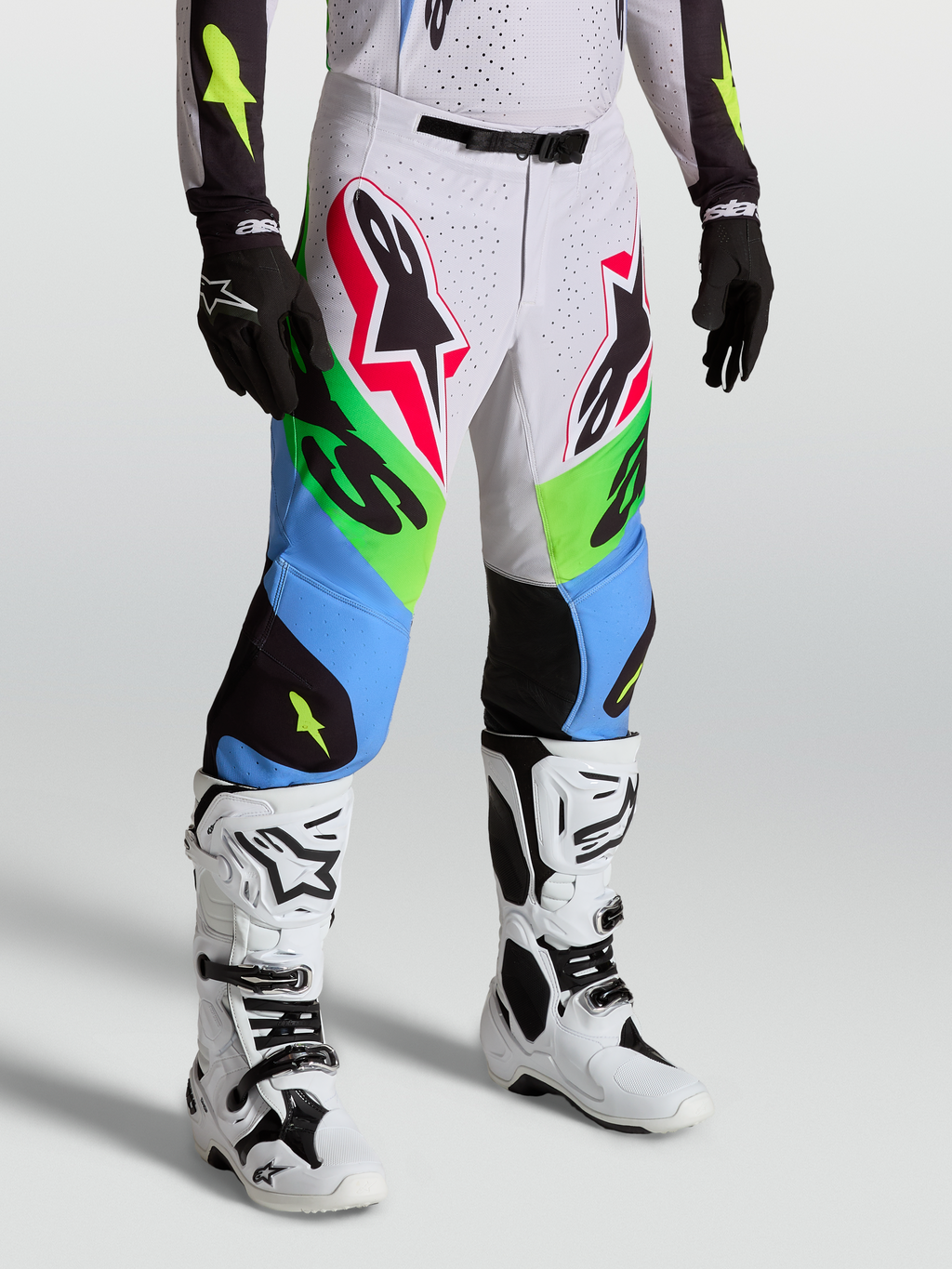 Alpinestars Pantaloni Supertech Dyna, pantaloni da motocross verdi e blu, indossati con stivali bianchi e guanti neri, abbigliamento racing professionale off-road