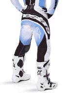 Alpinestars 2025 Techstar Melt Pants, pantaloni da motocross, nero, blu e bianco, vista posteriore con grande marchio Alpinestars sulla seduta e loghi a stella sulle gambe, indossati con stivali Tech 10 bianchi e neri, abbigliamento professionale da gara fuoristrada