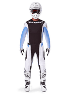 Pilota di motocross che indossa pantaloni Alpinestars 2025 Techstar Melt, pantaloni da motocross, nero e blu, design multi-pannello bianco e nero con accenti blu sui fianchi, indossati con maglia bianca coordinata, casco bianco, guanti bianchi e stivali per un kit completo da gara off-road