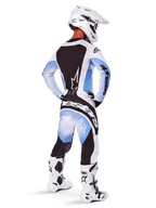 Pilota di motocross visto da dietro con maglia e pantaloni Alpinestars Techstar Melt 2025, design sfumato nero, blu e bianco, casco bianco, stivali bianchi e neri, kit completo da gara off-road