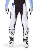 Alpinestars 2025 Techstar Melt Pants, pantaloni da motocross, bianco e nero con accenti azzurri, indossati con stivali e guanti coordinati in bianco e nero, caratterizzati da perforazioni tagliate al laser e design racing ad alte prestazioni.