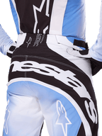 Pantaloni Alpinestars Techstar Melt 2025, pantaloni da motocross, nero, bianco e blu, vista posteriore ravvicinata con marchio bianco sulla seduta, coordinati con maglia e guanti Techstar Melt abbinati, abbigliamento professionale da gara per motocross