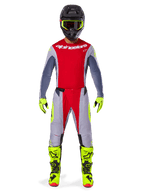 Pilota di motocross con pantaloni Alpinestars Techstar Melt 2025 in rosso brillante e grigio, caratterizzati da pannelli rossi vivaci e accenti giallo fluorescente, abbinati a maglia coordinata, casco nero con occhiali giallo fluorescente e stivali e guanti giallo brillante, completo coordinato per gare di motocross professionale.