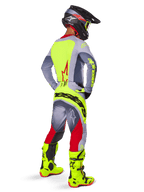 Pilota di motocross con Set Gear Alpinestars Techstar Melt 2025, visto dal retro, maglia grigia con pannello posteriore giallo neon e logo rosso, pantaloni grigi e rossi con marchio 'Alpinestars' giallo neon sulla seduta, stivali da motocross giallo neon e casco coordinato