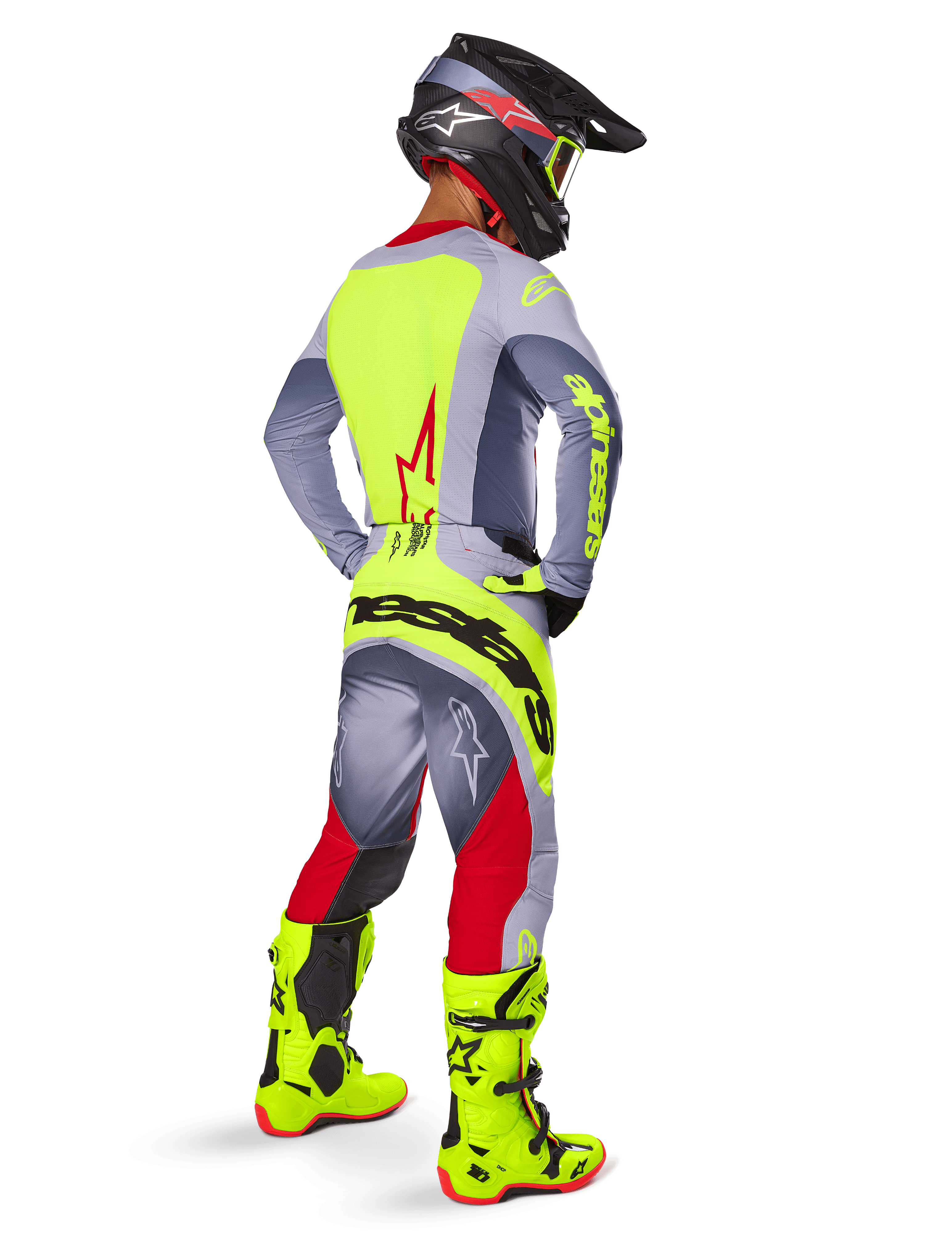 Pilota di motocross con Set Gear Alpinestars Techstar Melt 2025, visto dal retro, maglia grigia con pannello posteriore giallo neon e logo rosso, pantaloni grigi e rossi con marchio 'Alpinestars' giallo neon sulla seduta, stivali da motocross giallo neon e casco coordinato