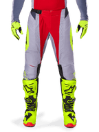 Alpinestars 2025 Techstar Melt Pants, pantaloni da motocross, rosso e grigio, con telaio grigio, pannelli centrali rossi e accenti laterali giallo neon, perforazioni tagliate al laser per la ventilazione, indossati con guanti e stivali giallo neon, equipaggiamento ad alte prestazioni per gare fuoristrada