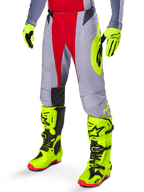 Alpinestars 2025 Techstar Melt Pants, pantaloni da motocross, rosso acceso e grigio, con grafiche laterali giallo neon e pannelli neri sulle ginocchia, abbinati a stivali e guanti giallo neon coordinati, progettati per prestazioni off-road competitive