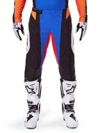 Pantaloni da motocross Alpinestars 2025 Techstar Melt, arancione e blu, indossati con maglia coordinata e stivali bianchi, caratterizzati da pannelli neri con accenti vivaci blu e arancioni, traforati per la ventilazione, vestibilità atletica da gara per prestazioni fuoristrada.