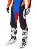 Alpinestars 2025 Techstar Melt Pants, pantaloni da motocross, nero con accenti blu e arancione, indossati con stivali bianchi e maglia coordinata, caratterizzati da materiale protettivo resistente e un design sportivo da gara