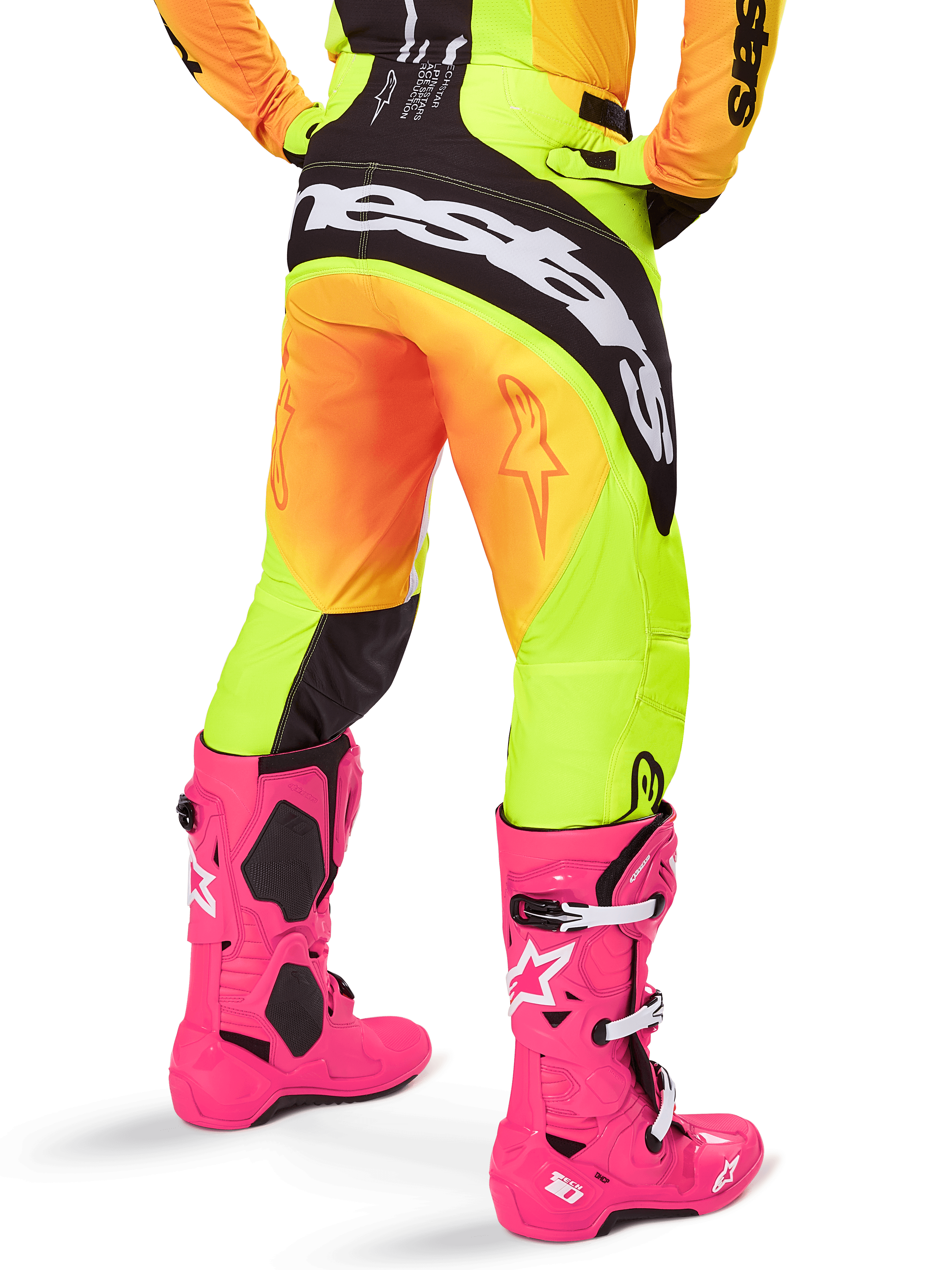 Vista posteriore di un pilota di motocross che indossa i pantaloni Alpinestars 2025 Techstar Melt, sfumatura gialla e arancione con logo nero e bianco sulla seduta, abbinati a stivali da motocross rosa acceso, abbigliamento tecnico da fuoristrada