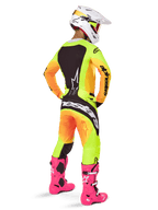 Pilota di motocross visto da dietro con il completo Alpinestars 2025 Techstar Melt, maglia e pantaloni con sfumatura giallo e arancione e pannelli neri, casco bianco con occhiali rossi e stivali rosa acceso, abbigliamento da corsa coordinato per prestazioni fuoristrada