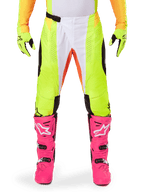 Alpinestars 2025 Techstar Melt Pants, pantaloni da motocross, giallo neon e bianco con accenti arancioni, indossati con guanti gialli coordinati e stivali da motocross rosa acceso, pannelli di ventilazione traforati e fibbia magnetica in vita, attrezzatura da gara ad alte prestazioni.